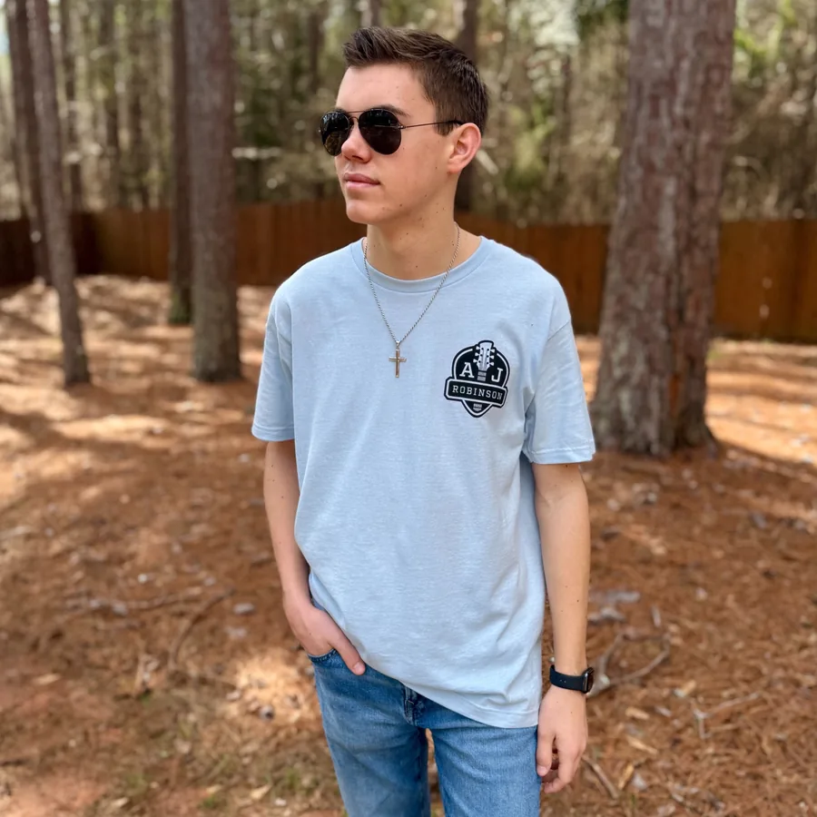 AJ wearing a light blue tee with the crest on the chest, in the Georgia pines