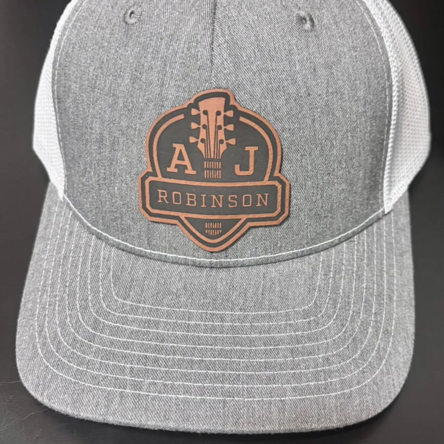 Heather gray and white trucker hat with the AJ Robinson crest on a leather patch